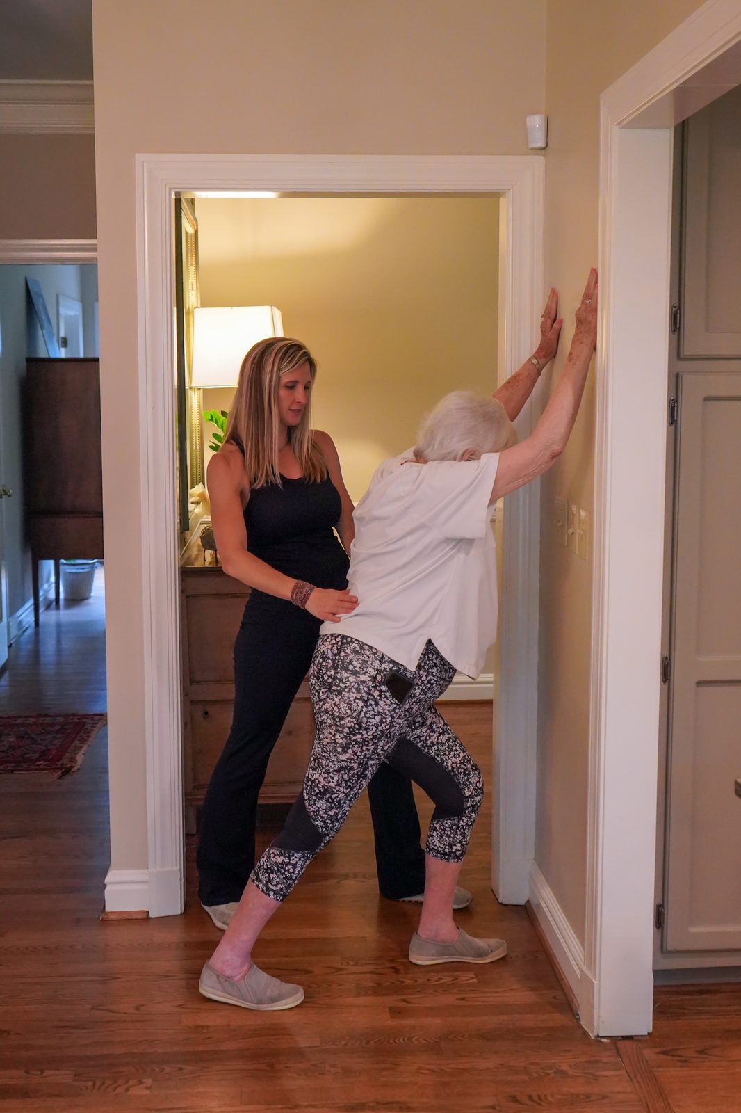 Trainer guiding an older adult through a supported standing calf stretch against a wall