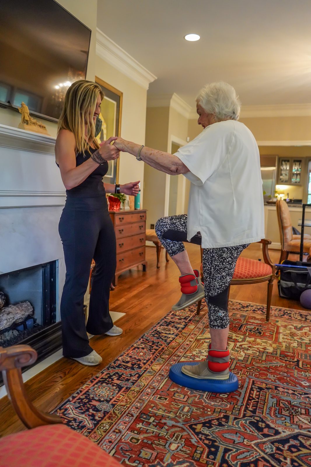 An older adult balancing on a stability pad while the trainer steadies her hands