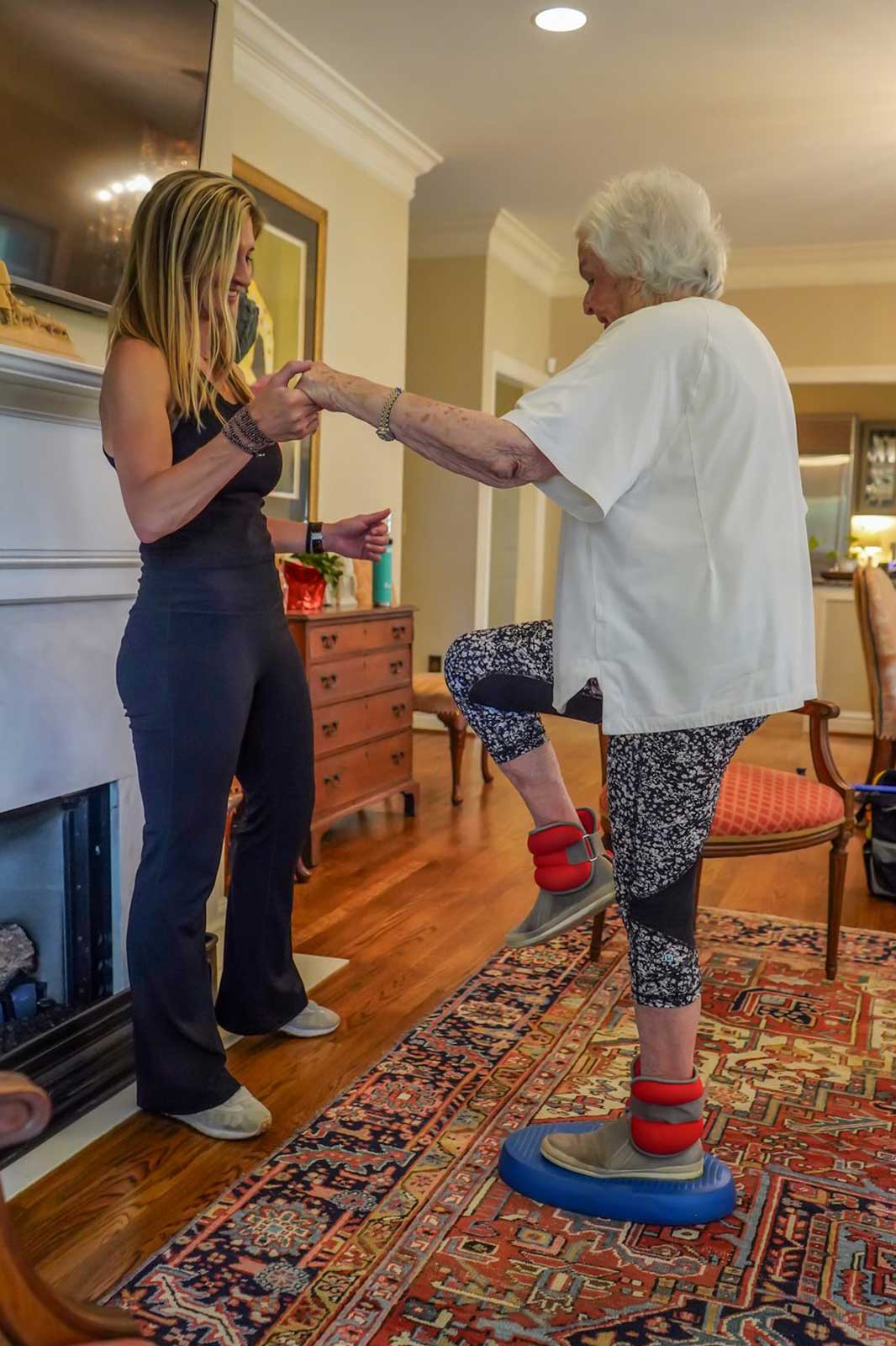 A Graceful Aging trainer guiding an older adult through a seated resistance-band leg exercise in her Birmingham home